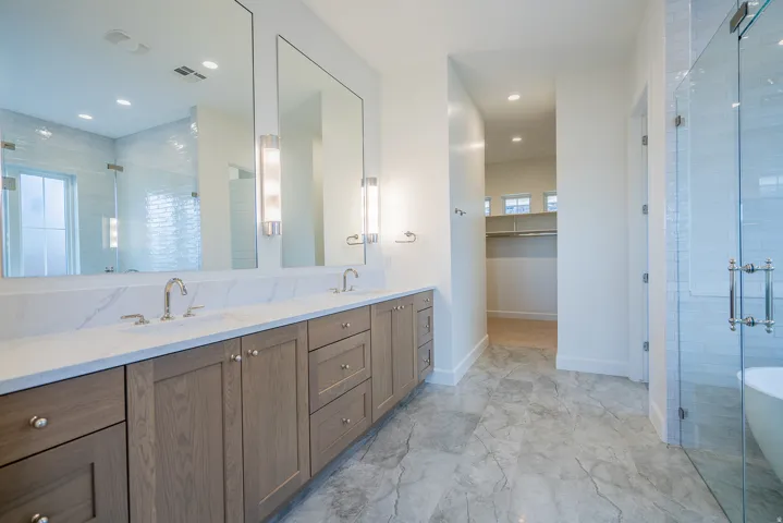 Bathroom featuring a shower stall, double vanity, a spacious closet, recessed lighting, and light marble finish flooring