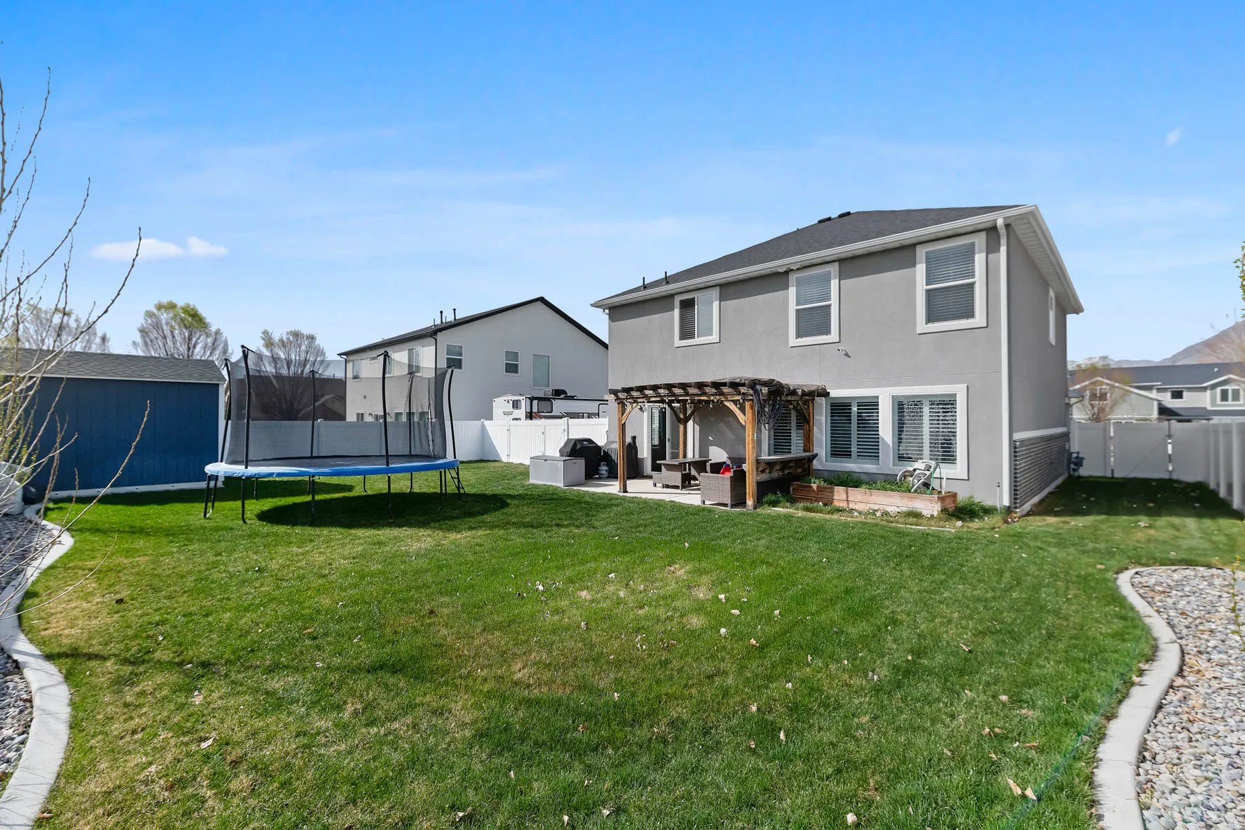 Rear view of property featuring a patio, a pergola, stucco siding, a trampoline, and a fenced backyard