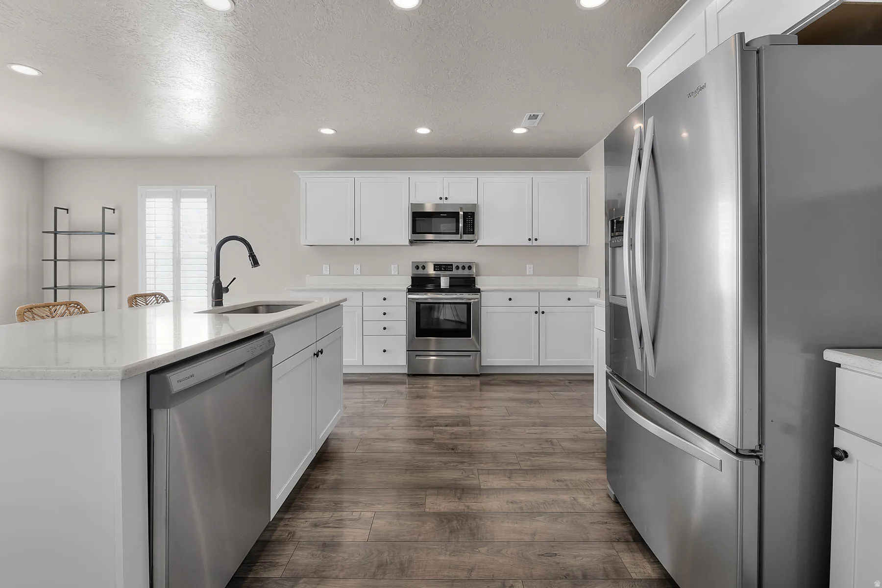 Kitchen with stainless steel appliances, white cabinetry, a kitchen island with sink, a textured ceiling, and recessed lighting