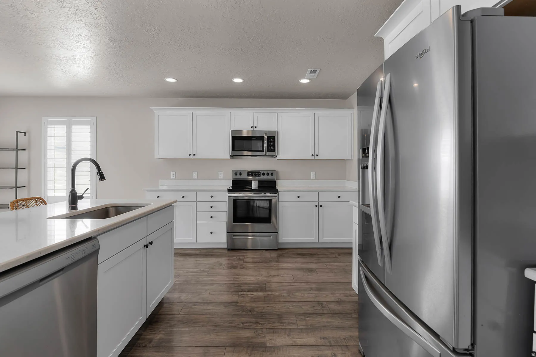 Kitchen featuring stainless steel appliances, white cabinetry, recessed lighting, a textured ceiling, and dark wood finished floors