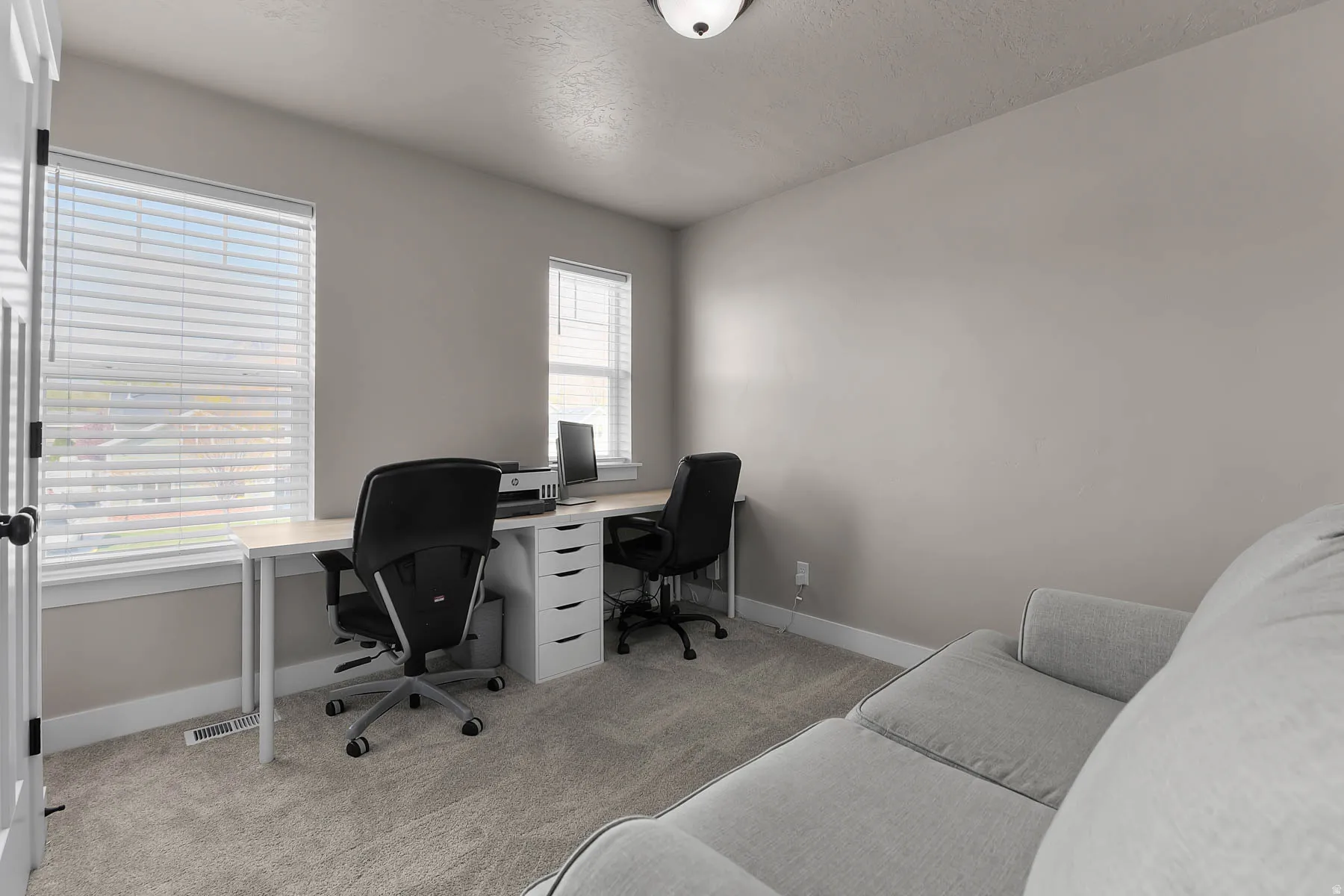 Office space with light colored carpet and a textured ceiling