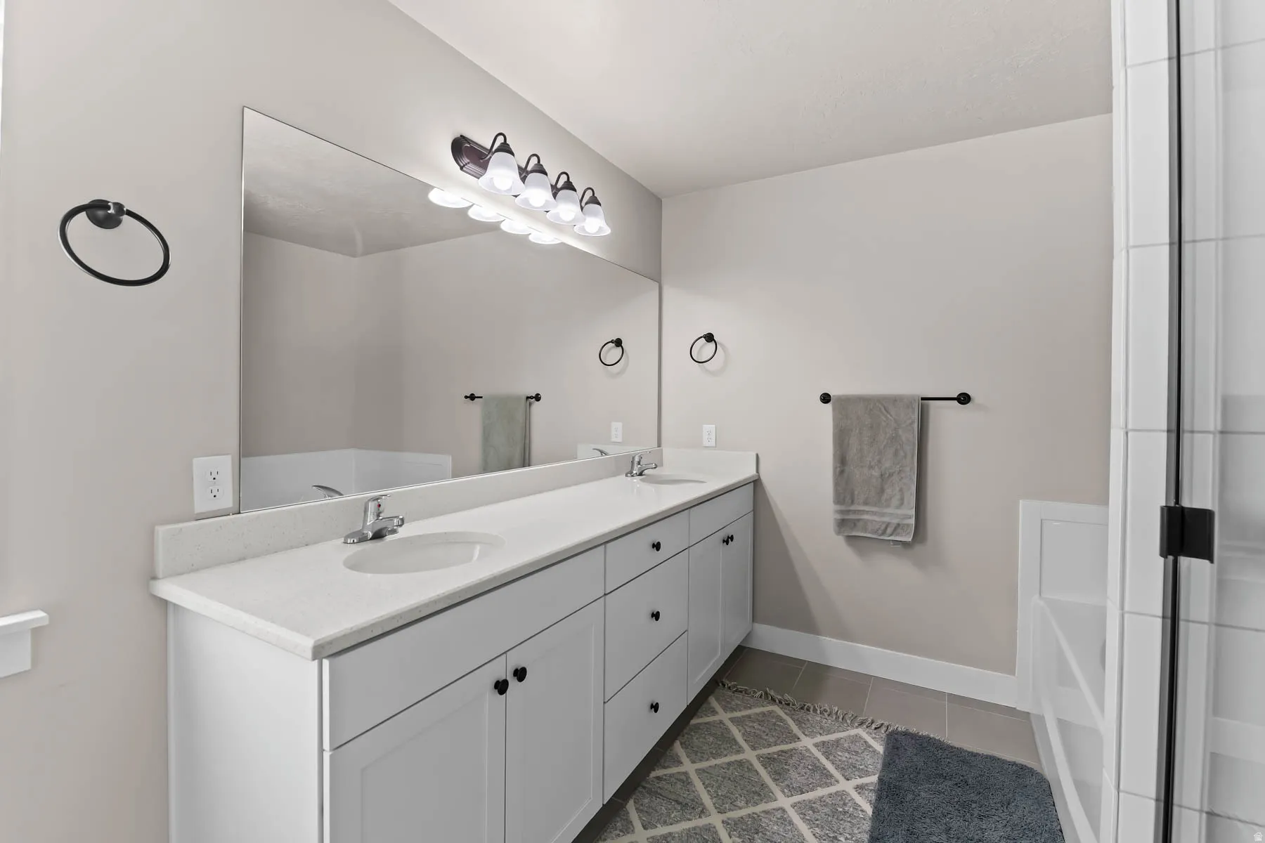 Bathroom with double vanity, a garden tub, and dark tile patterned floors