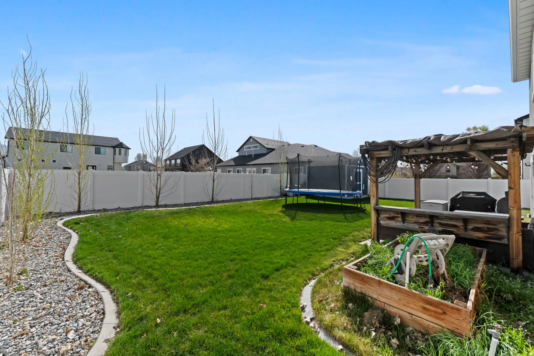 Fenced backyard with a garden, a residential view, a pergola, and a trampoline