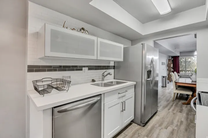 Kitchen featuring white cabinetry, stainless steel appliances, light wood-style floors, decorative backsplash, and a tray ceiling