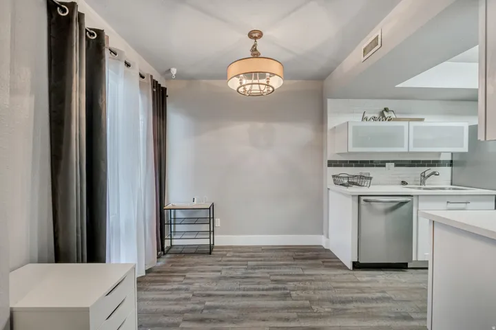 Kitchen featuring white cabinets, stainless steel dishwasher, backsplash, hanging light fixtures, and light wood finished floors