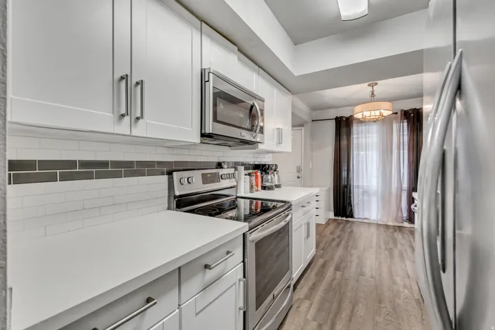 Kitchen featuring stainless steel appliances, white cabinetry, light countertops, and light wood-style floors