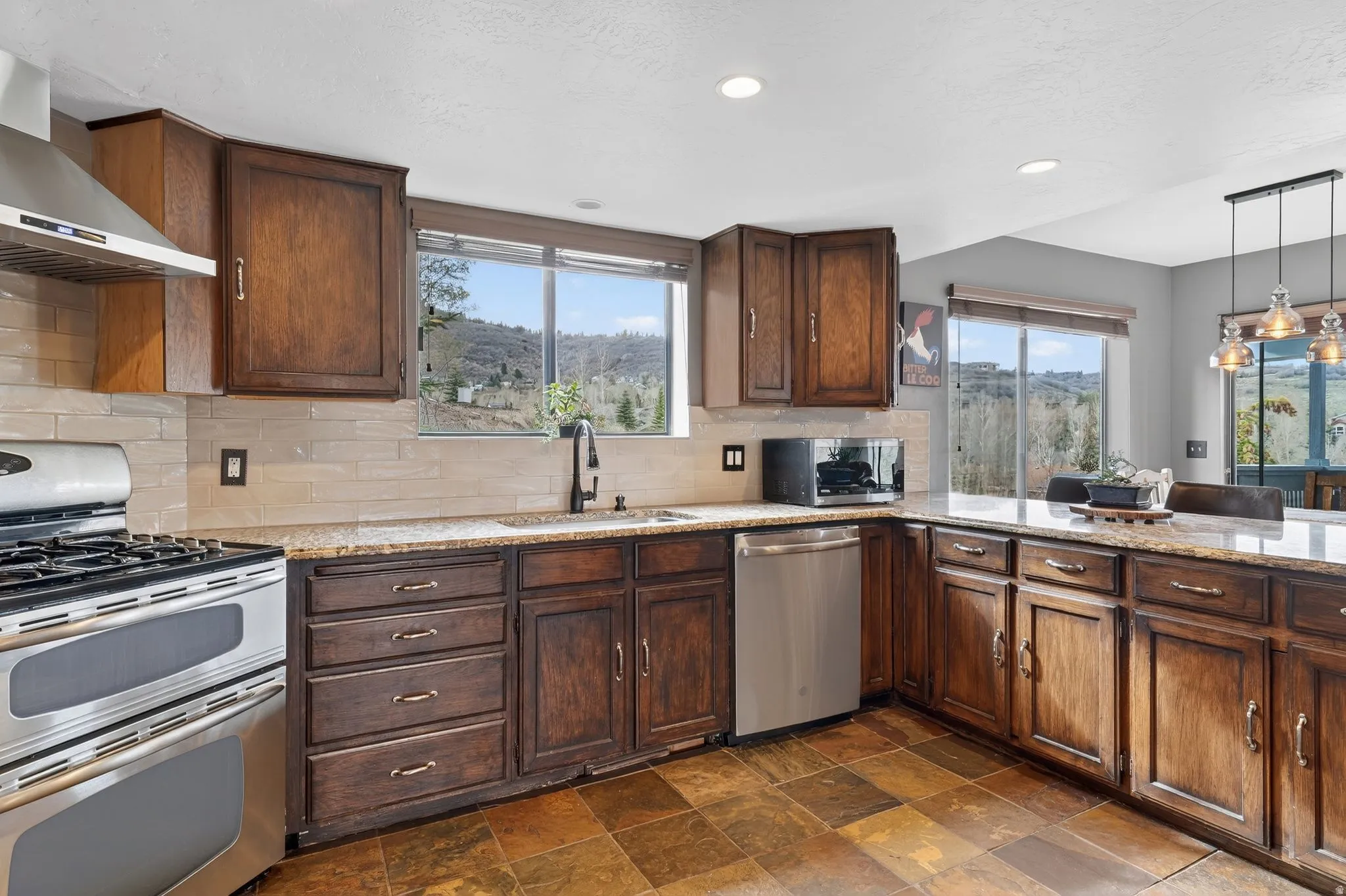 Kitchen featuring stainless steel appliances, light stone countertops, dark stone finish floors, and tasteful backsplash