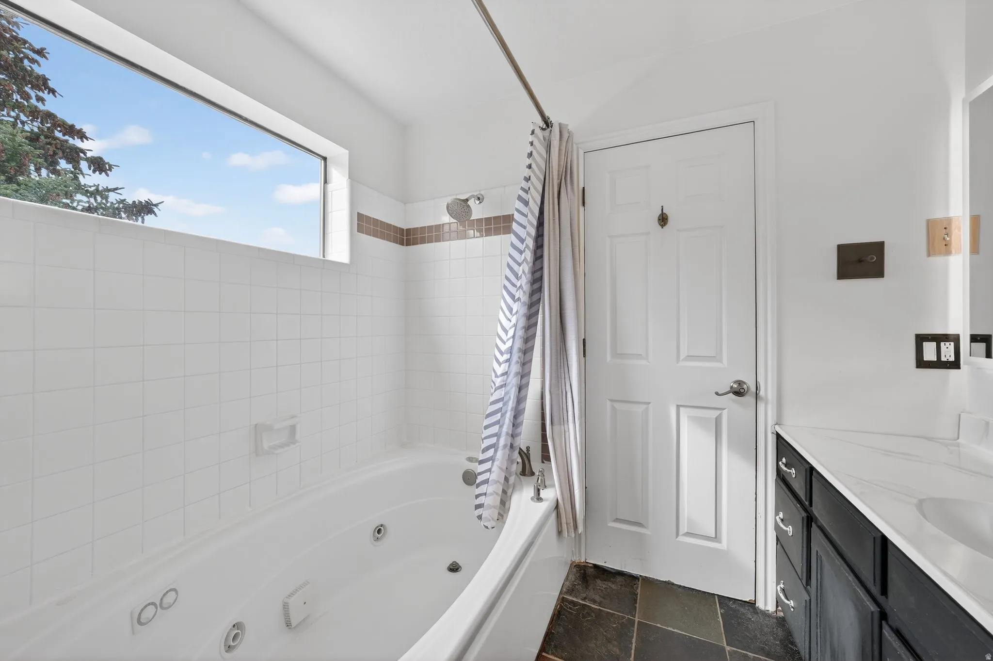 Bathroom with a combined bath / shower with jetted tub, vanity, and dark stone finish flooring