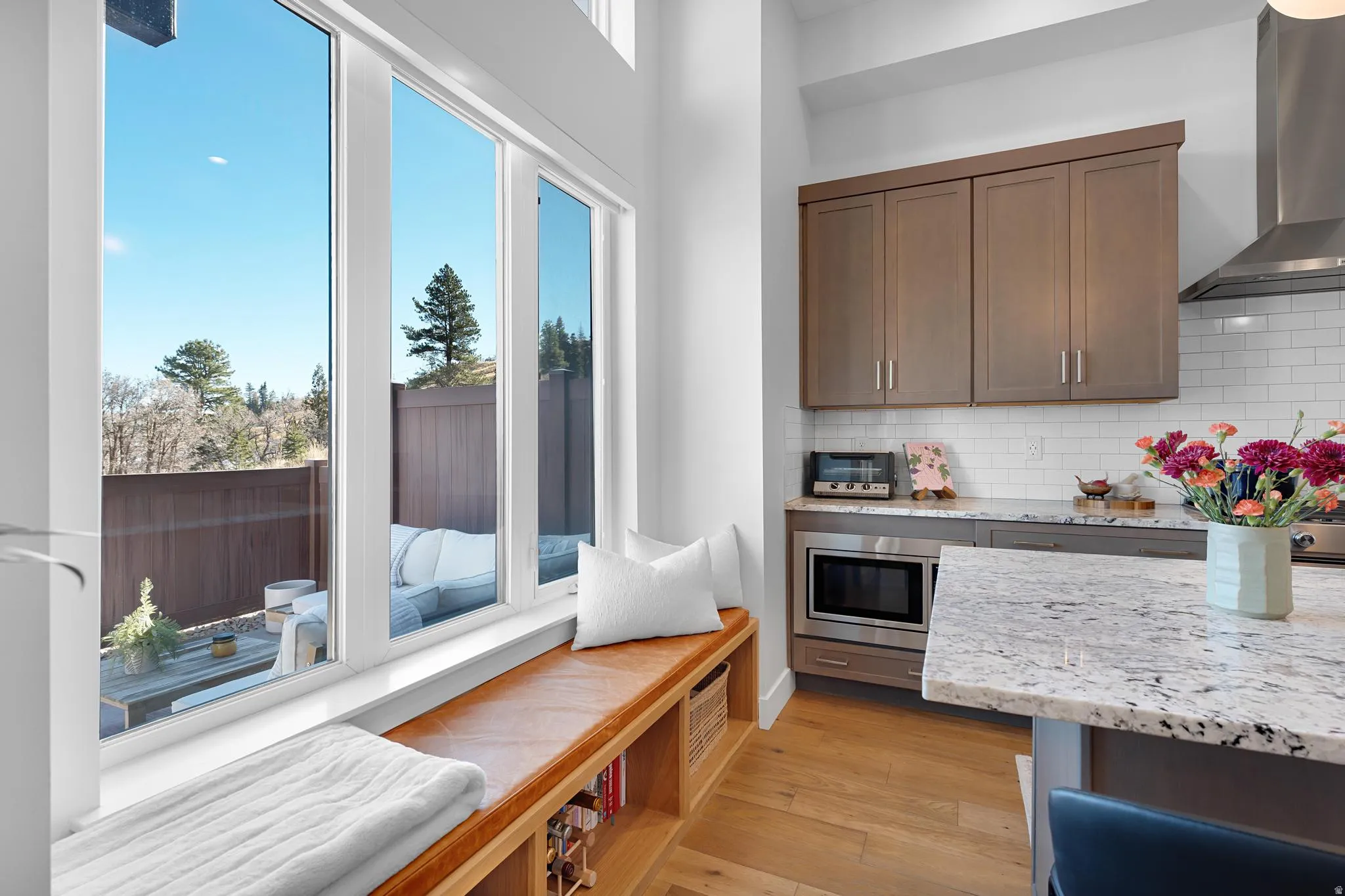 Kitchen with light stone countertops, light wood finished floors, tasteful backsplash, stainless steel microwave, and dark wood finish cabinets