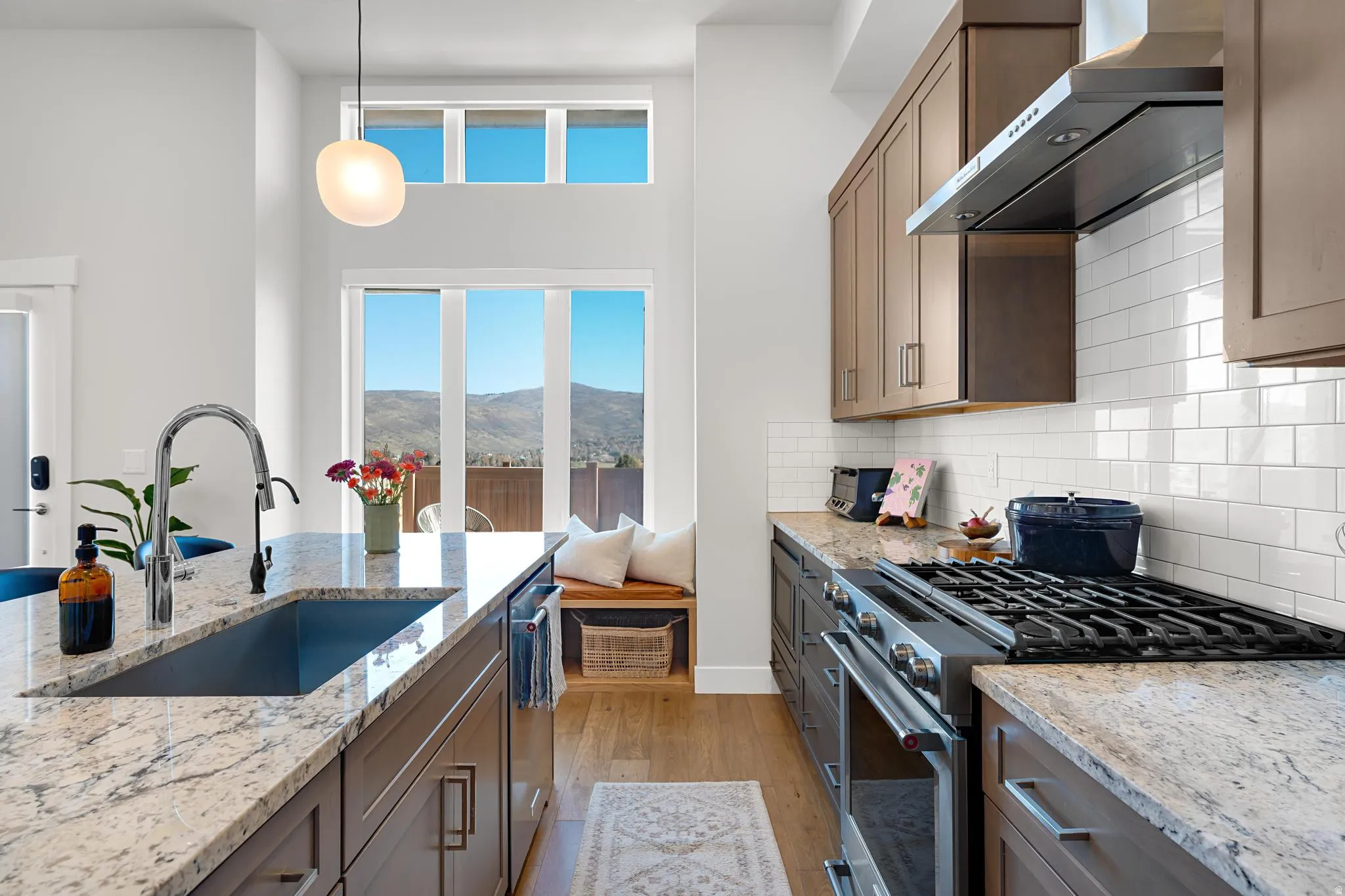 Kitchen featuring stainless steel appliances, light wood-style floors, light stone counters, hanging light fixtures, and decorative backsplash