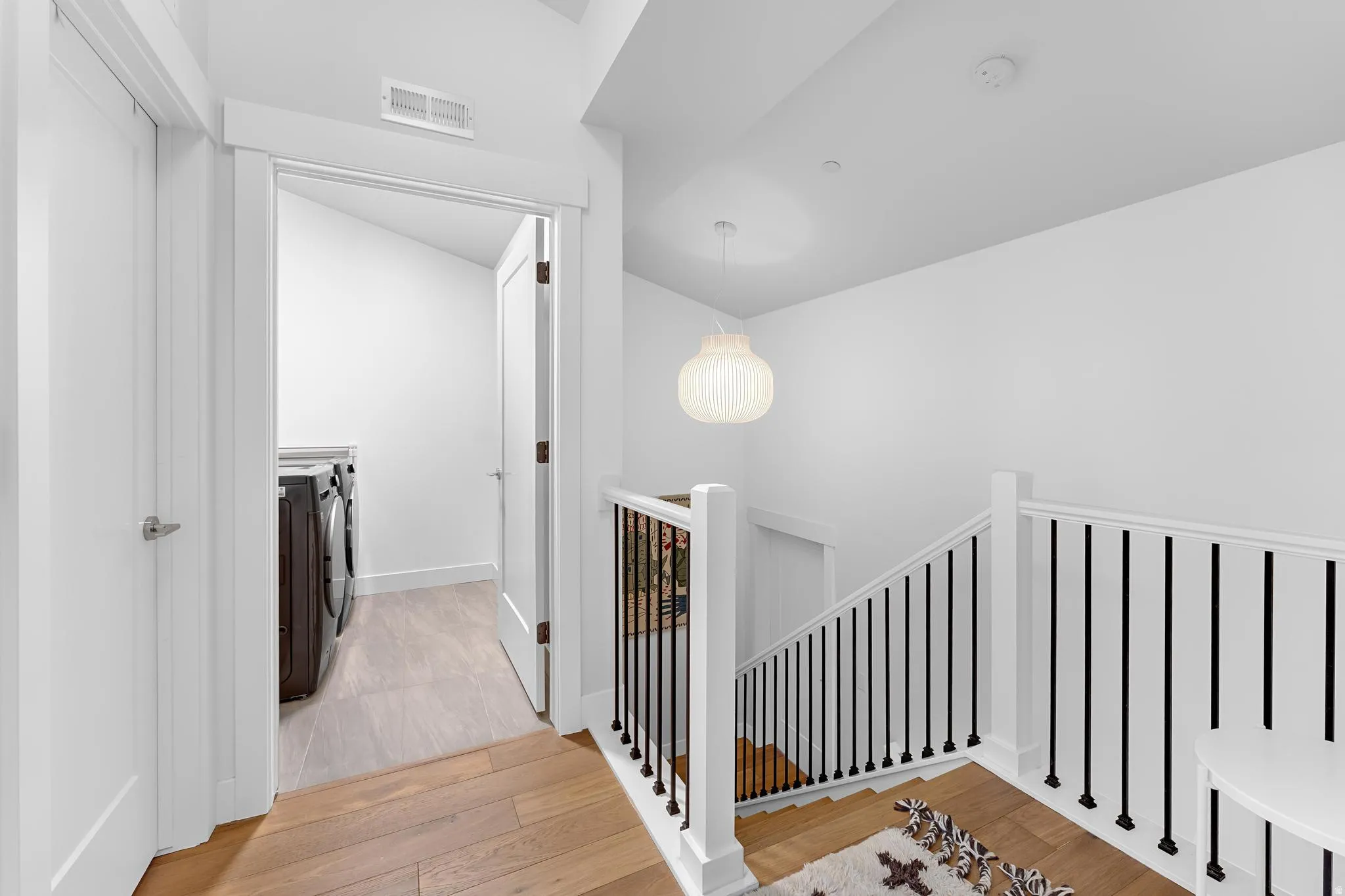 Hallway with light wood-style floors, separate washer and dryer, an upstairs landing, and vaulted ceiling