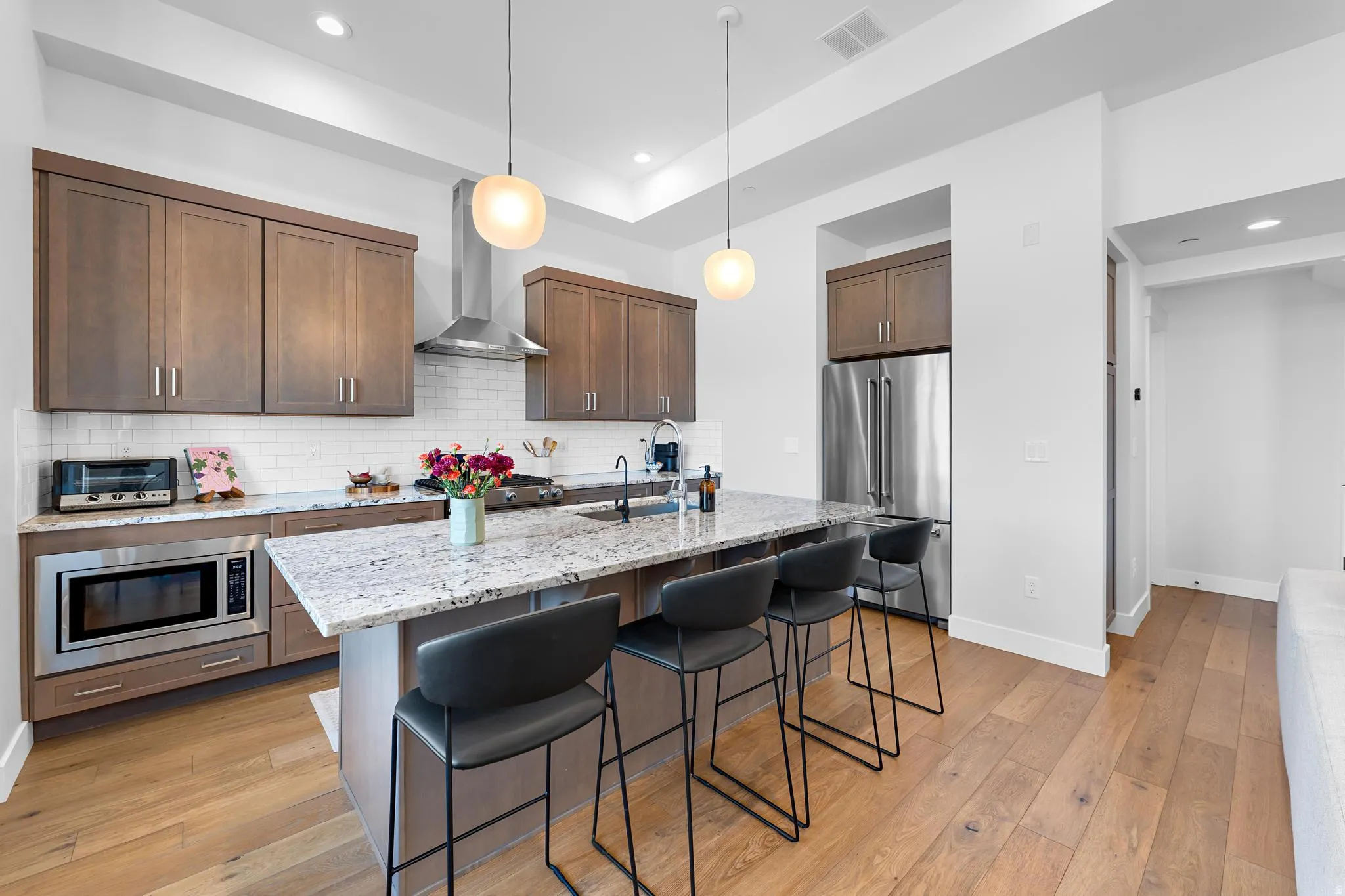 Kitchen featuring light stone countertops, a kitchen island with sink, stainless steel appliances, dark wood finish cabinets, and hanging light fixtures