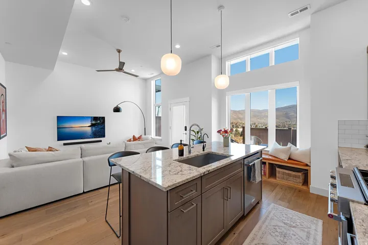 Kitchen featuring pendant lighting, light stone countertops, a center island with sink, light wood-type flooring, and stainless steel appliances