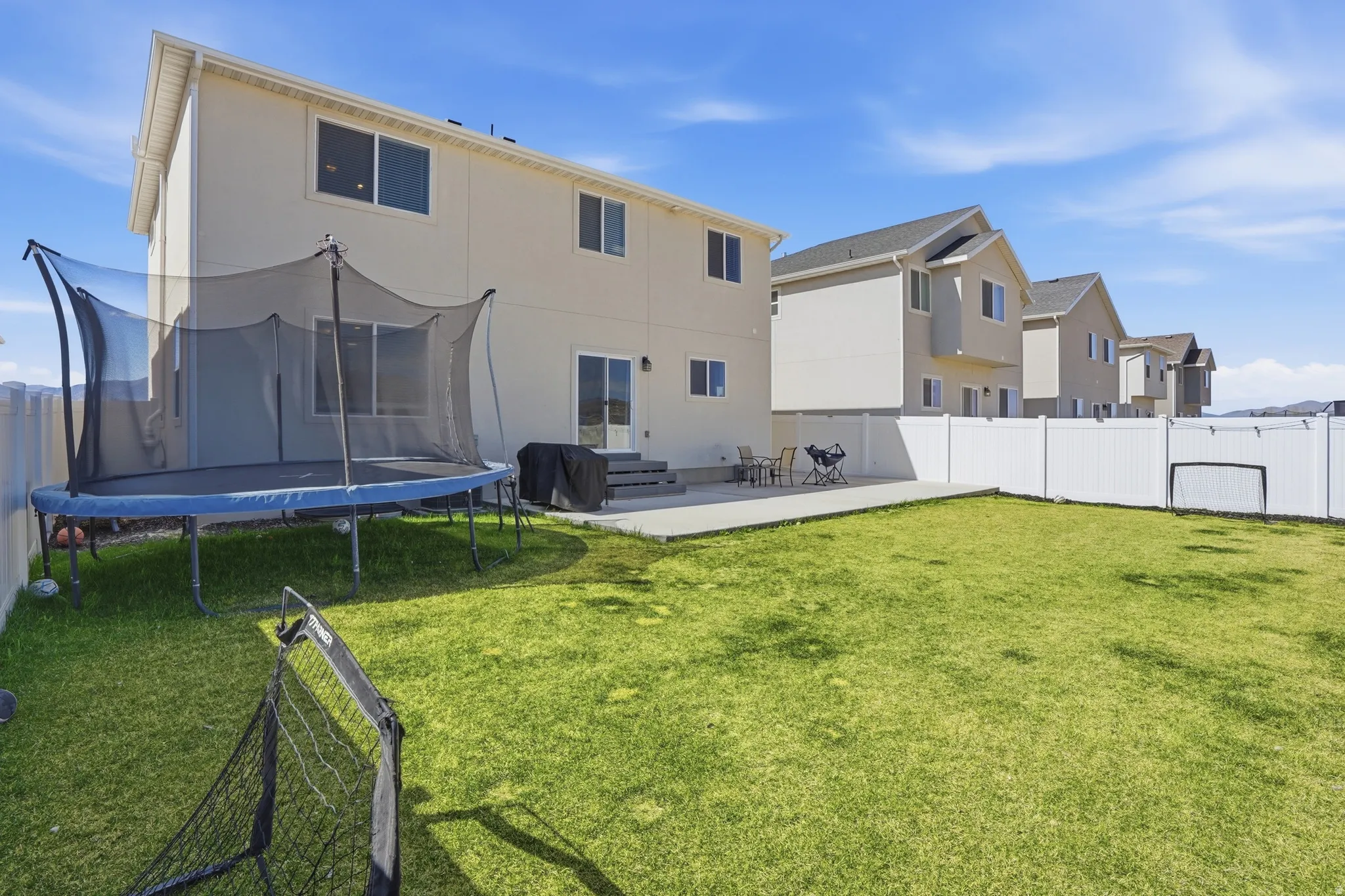Rear view of property featuring a patio area, a fenced backyard, a trampoline, and stucco siding