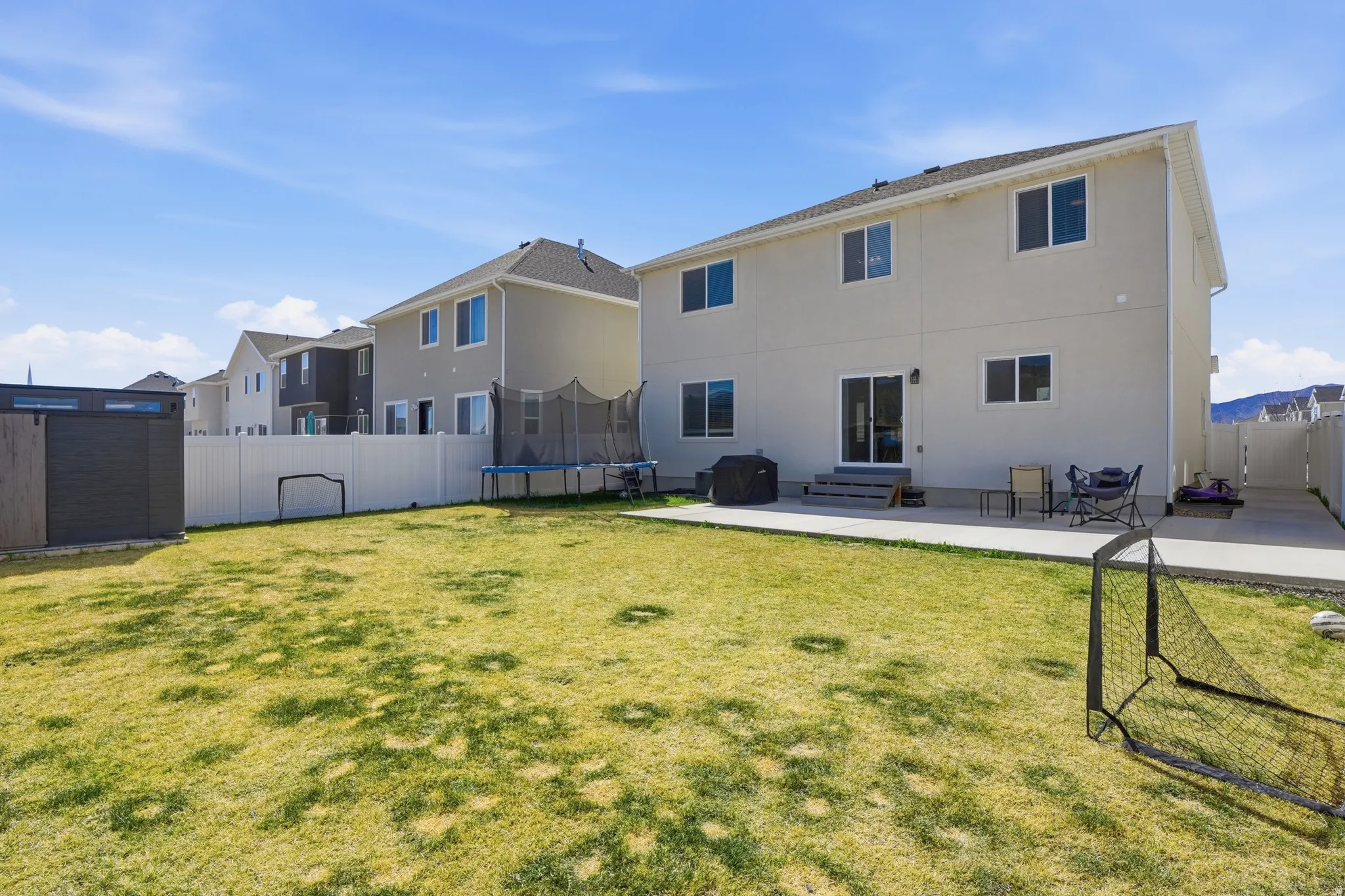 Rear view of house with a patio area, a trampoline, a fenced backyard, entry steps, and stucco siding