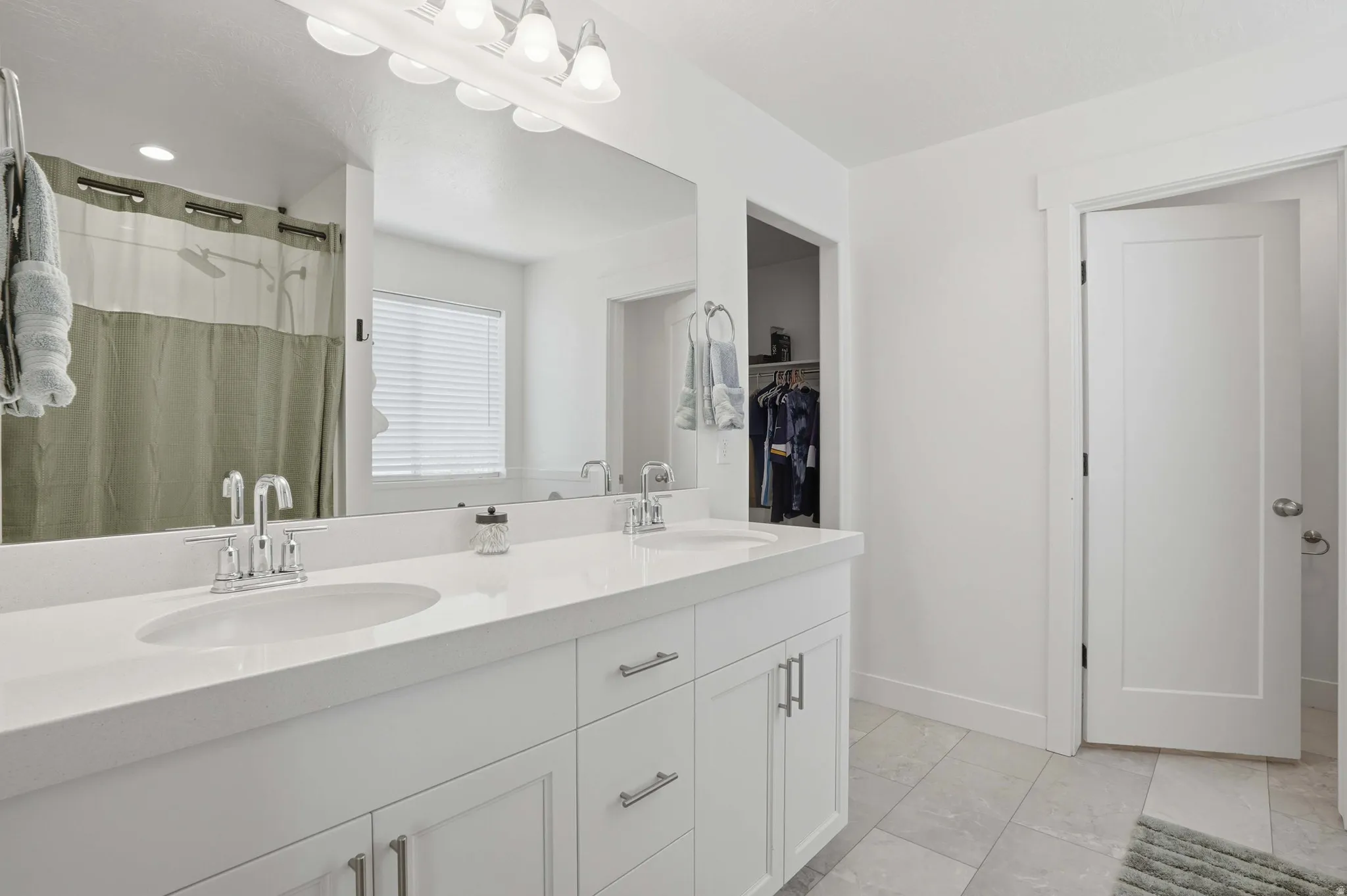Bathroom with double vanity, a shower with shower curtain, and light marble finish floors