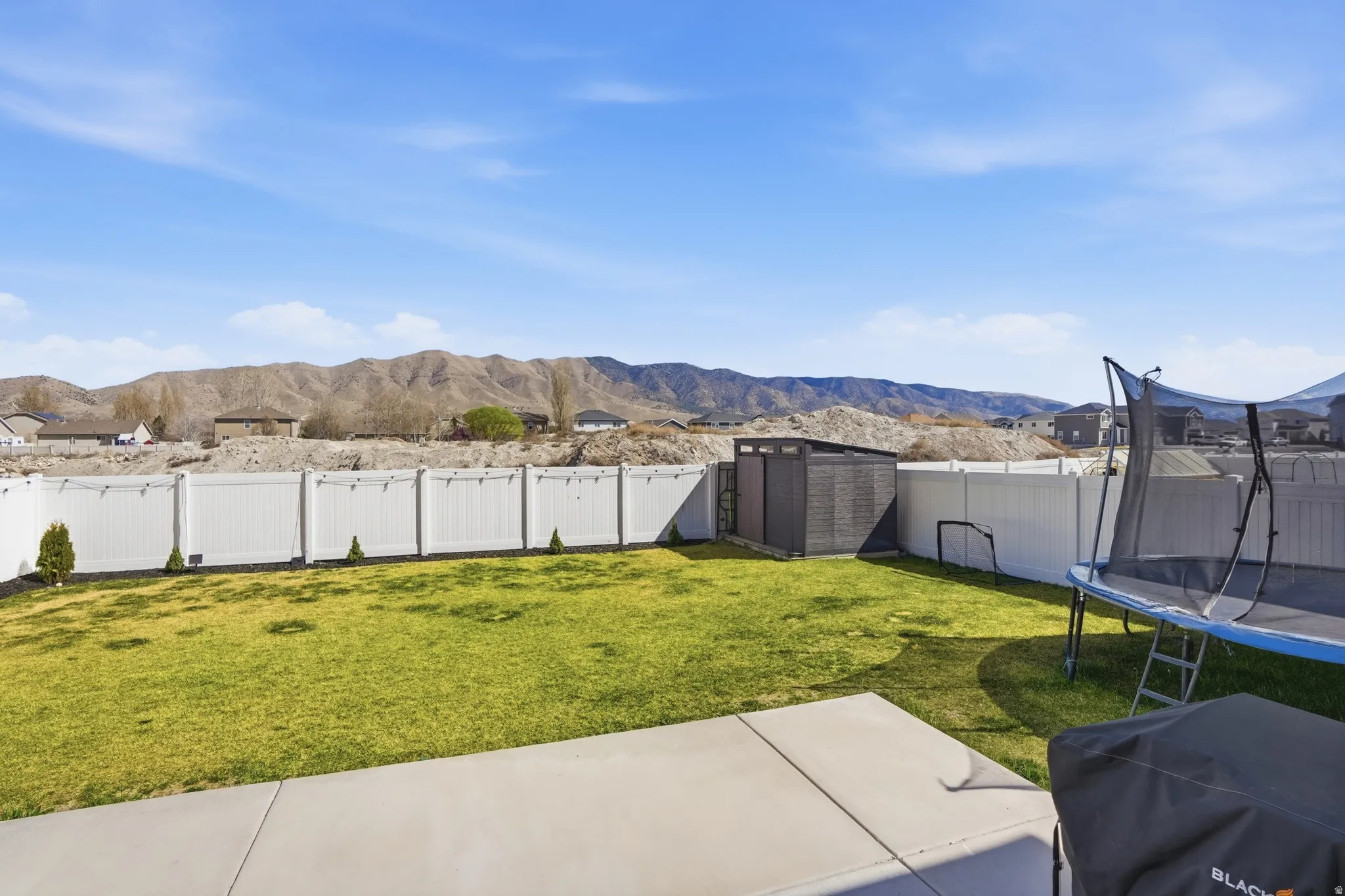 Fenced backyard featuring a shed, a mountain view, a trampoline, and a patio area