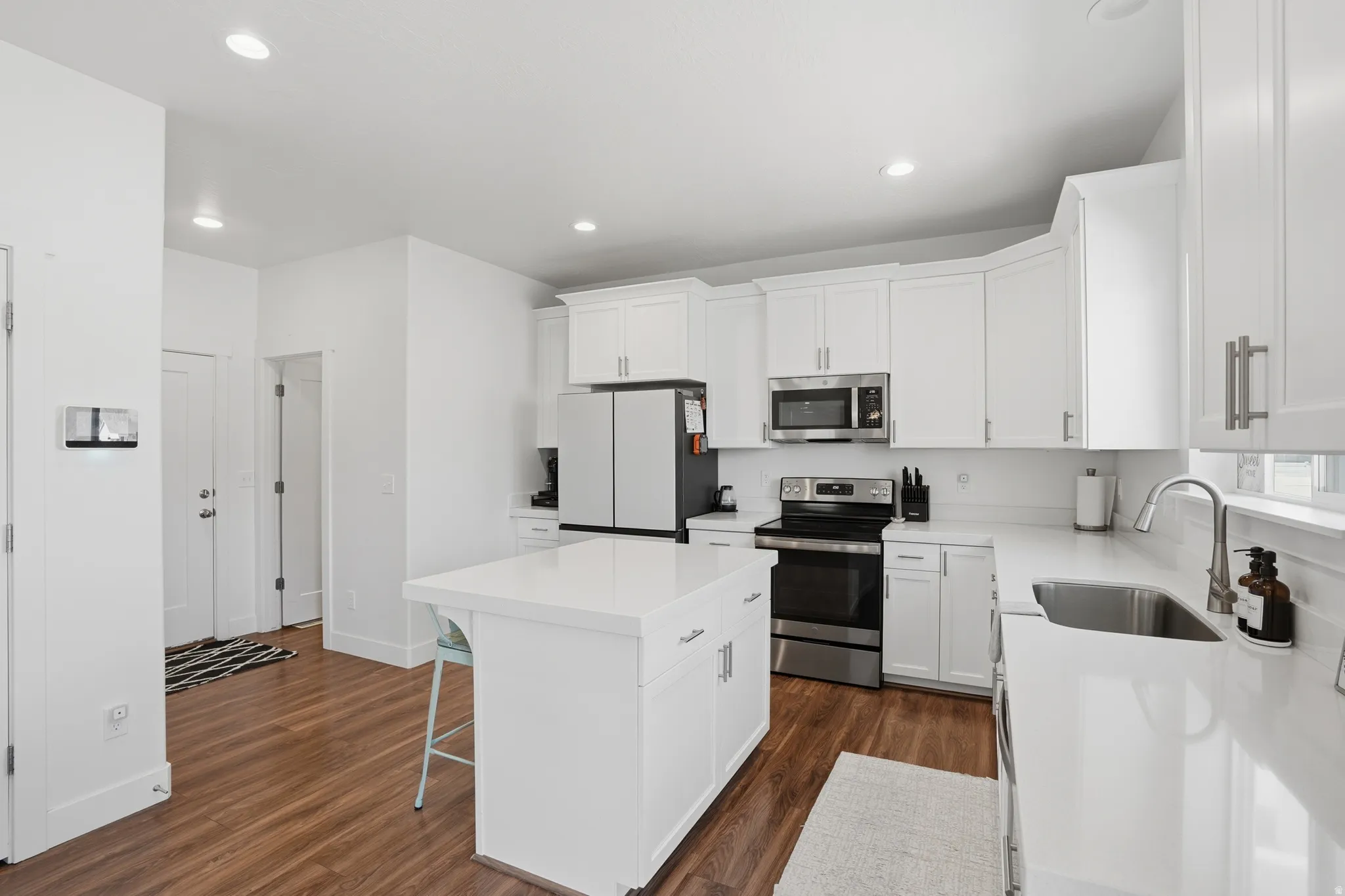 Kitchen with stainless steel appliances, white cabinets, a center island, a breakfast bar area, and dark wood-type flooring