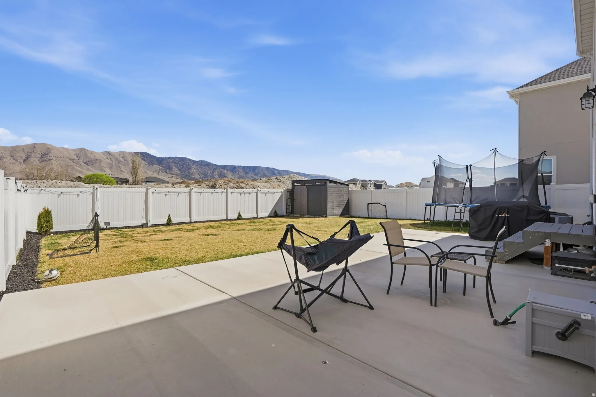 Fenced backyard featuring a shed, a mountain view, a patio area, and a trampoline
