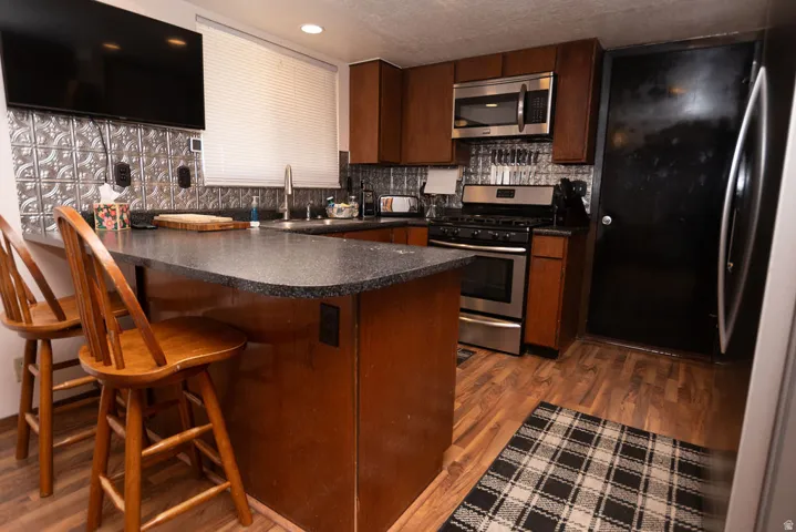 Kitchen with a peninsula, dark countertops, stainless steel appliances, and dark wood finished floors