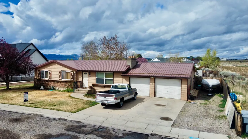 Ranch-style house featuring concrete driveway, an attached garage, a standing seam roof, a chimney, and a mountain view