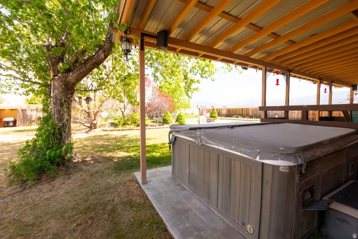 Covered hot tub area featuring a concrete slab foundation, wood-framed overhead structure with a metal roof, and a mature tree providing natural shade