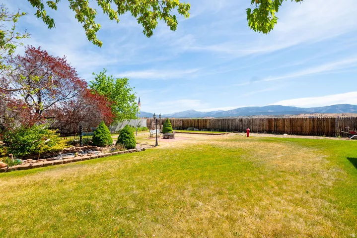 Expansive backyard featuring a partial wood fence, landscaped garden beds with mature trees, and a mountain backdrop