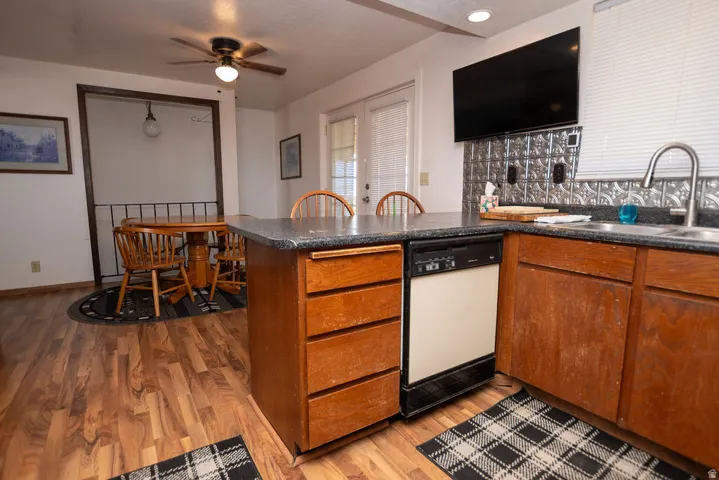 Kitchen featuring a peninsula, dark countertops, dishwasher, and light wood-style floors