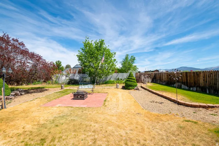 Expansive backyard featuring a red paver patio, a partial wooden privacy fence, a gravel pathway with brick edging, and mature trees