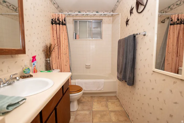 Bathroom with wallpapered walls, vanity, shower / tub combo with curtain, and light tile patterned floors