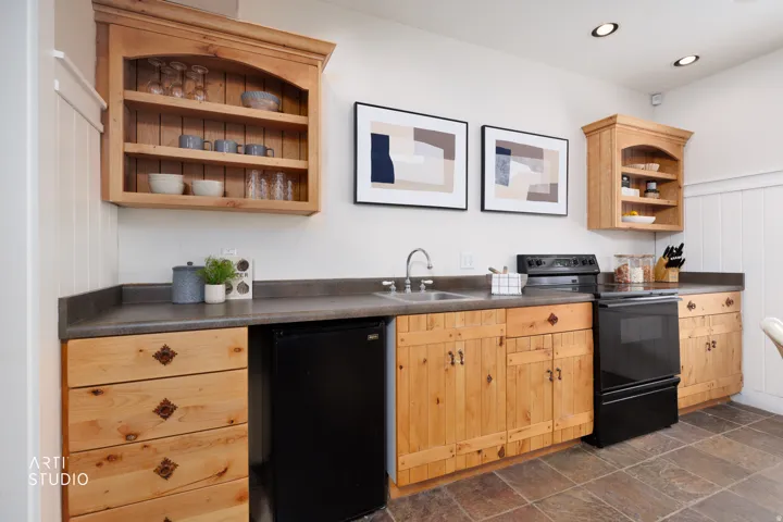 Kitchen featuring open shelves, dark countertops, black appliances, stone tile flooring, and light wood finish cabinets