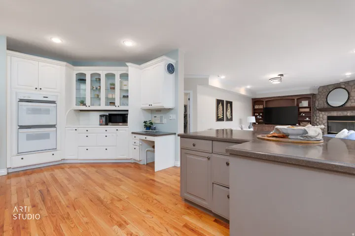 Kitchen with dark countertops, glass fronted cabinets, open floor plan, white double oven, and light wood finished floors