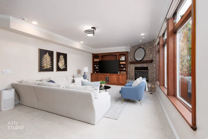 Living room with a stone fireplace, light carpet, healthy amount of natural light, ornamental molding, and recessed lighting