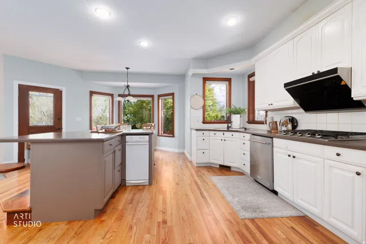 Kitchen with light wood-type flooring, dark countertops, hanging light fixtures, stainless steel appliances, and ventilation hood