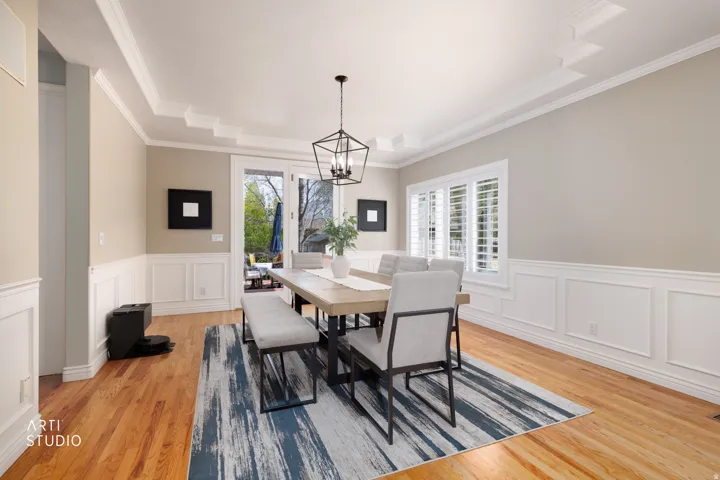 Dining room featuring wainscoting, suspended lighting, light wood-style floors, a decorative wall, and crown molding