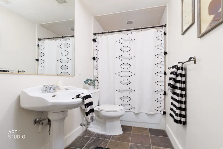 Full bath featuring shower / bath combo with shower curtain and dark stone finish flooring