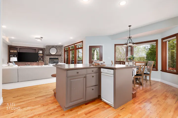Kitchen with a kitchen island with sink, open floor plan, light wood-type flooring, and a stone fireplace