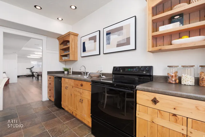 Kitchen with open shelves, black appliances, dark countertops, dark stone finish flooring, and light wood finish cabinetry