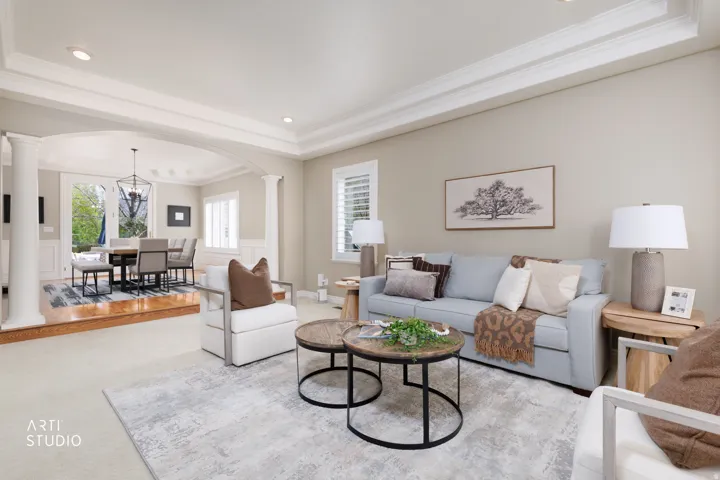 Carpeted living room featuring decorative columns, a tray ceiling, arched walkways, ornamental molding, and hanging lights