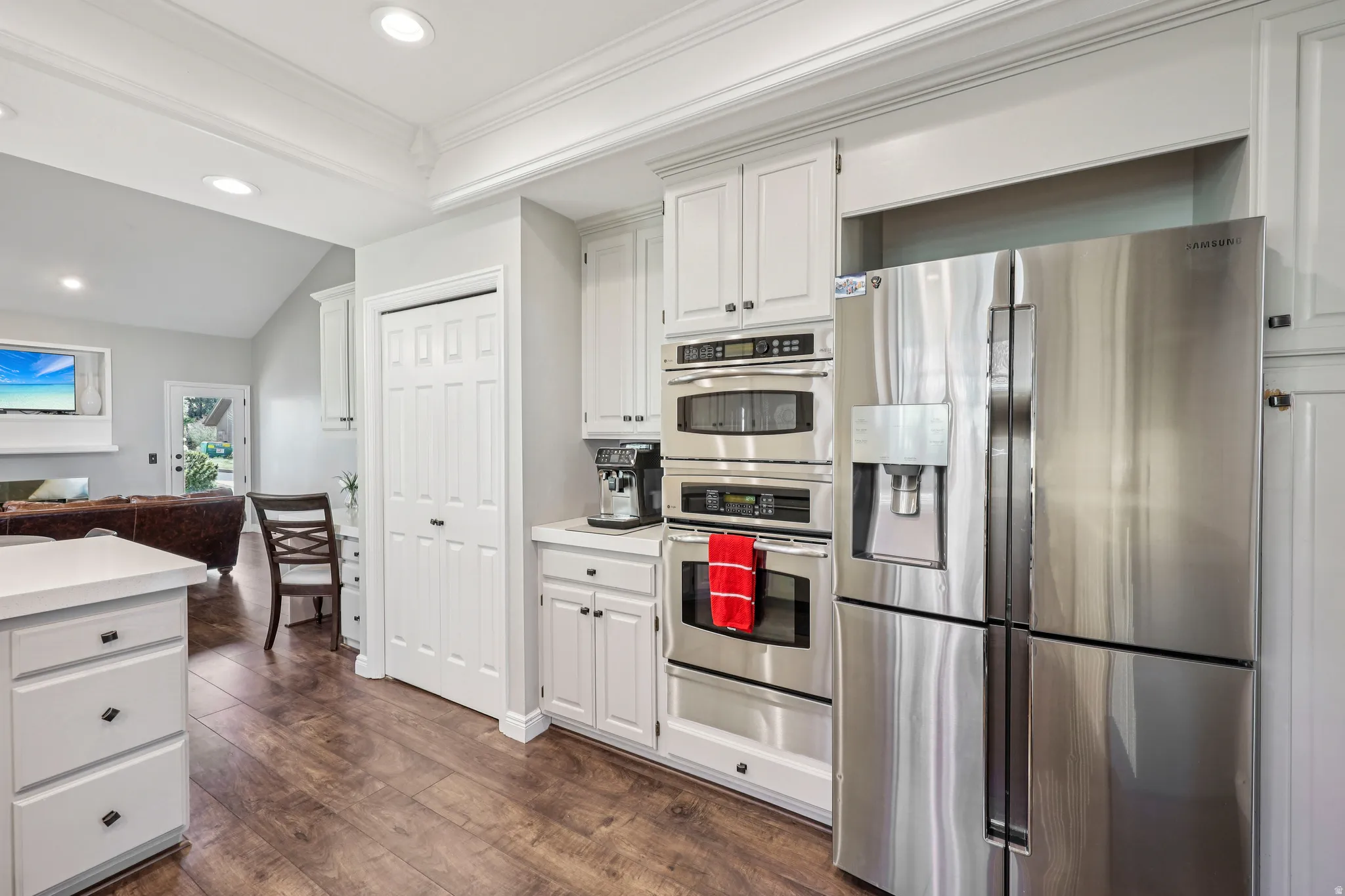 Kitchen featuring stainless steel appliances, light countertops, vaulted ceiling, dark wood-type flooring, and white cabinetry