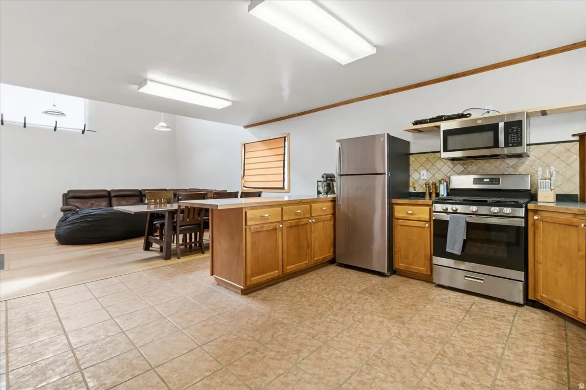 Kitchen with a peninsula, stainless steel appliances, ornamental molding, wood finish cabinetry, and decorative backsplash