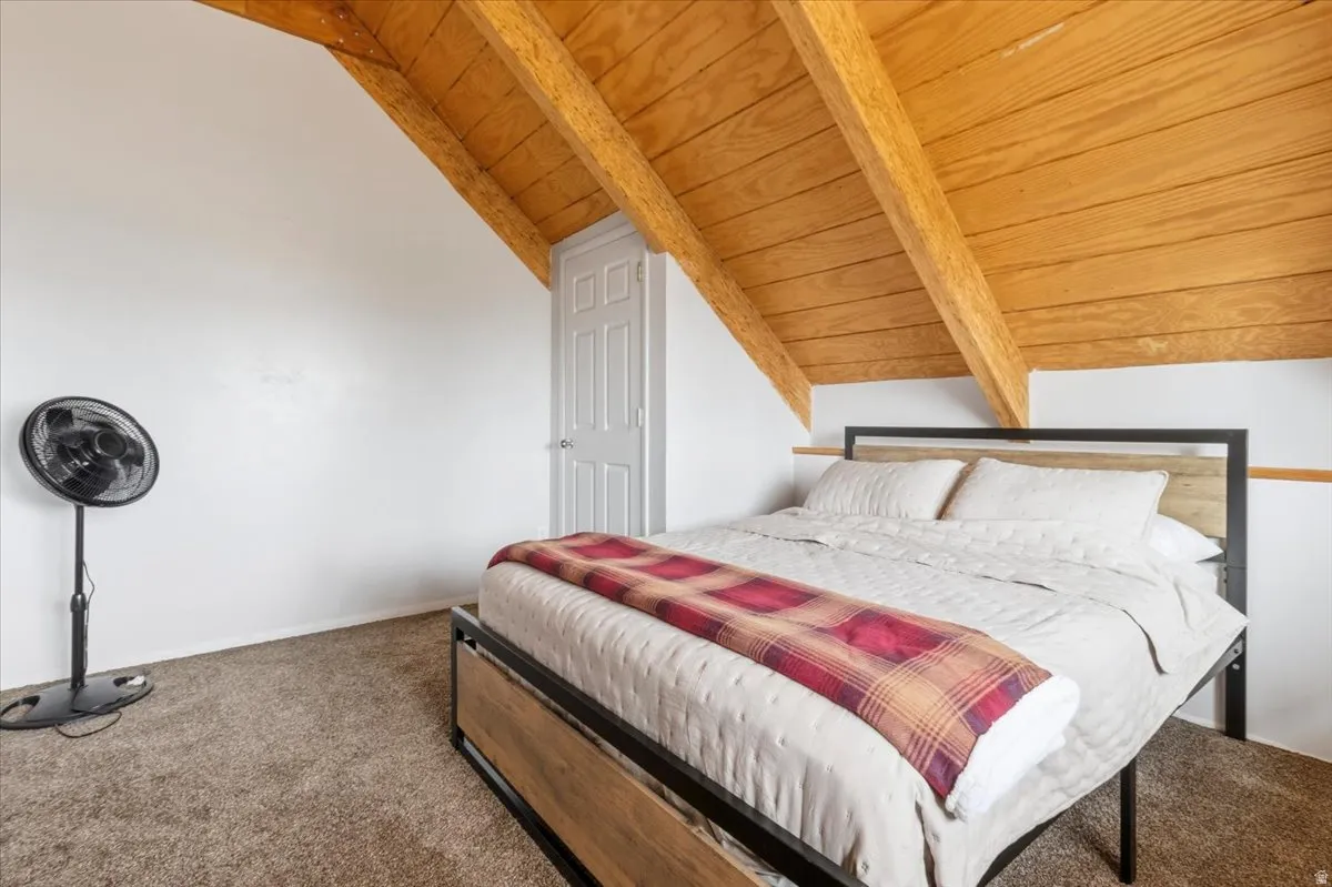 Carpeted bedroom featuring lofted ceiling with beams and wood ceiling