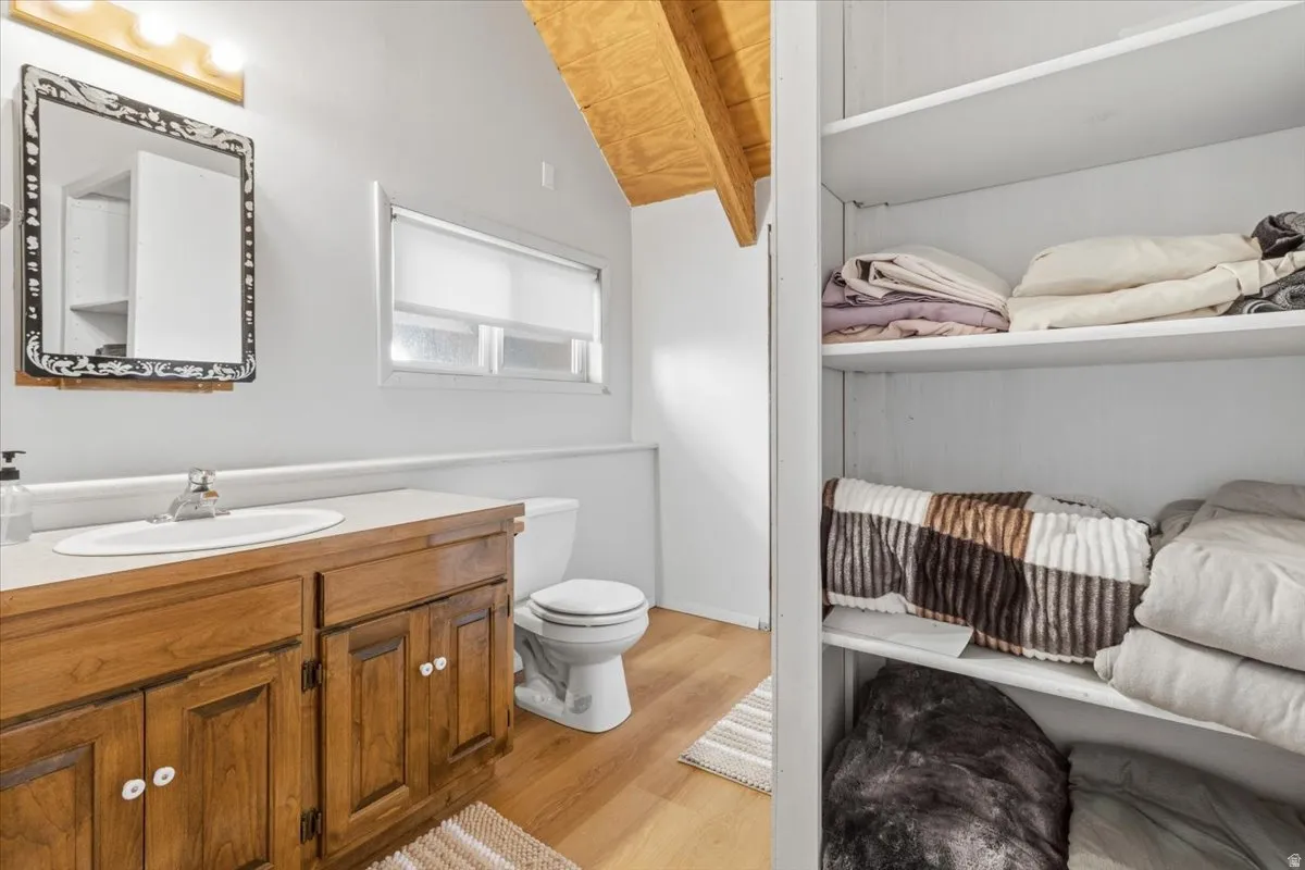 Half bathroom featuring vanity, light wood-style floors, wooden ceiling, and lofted ceiling with beams