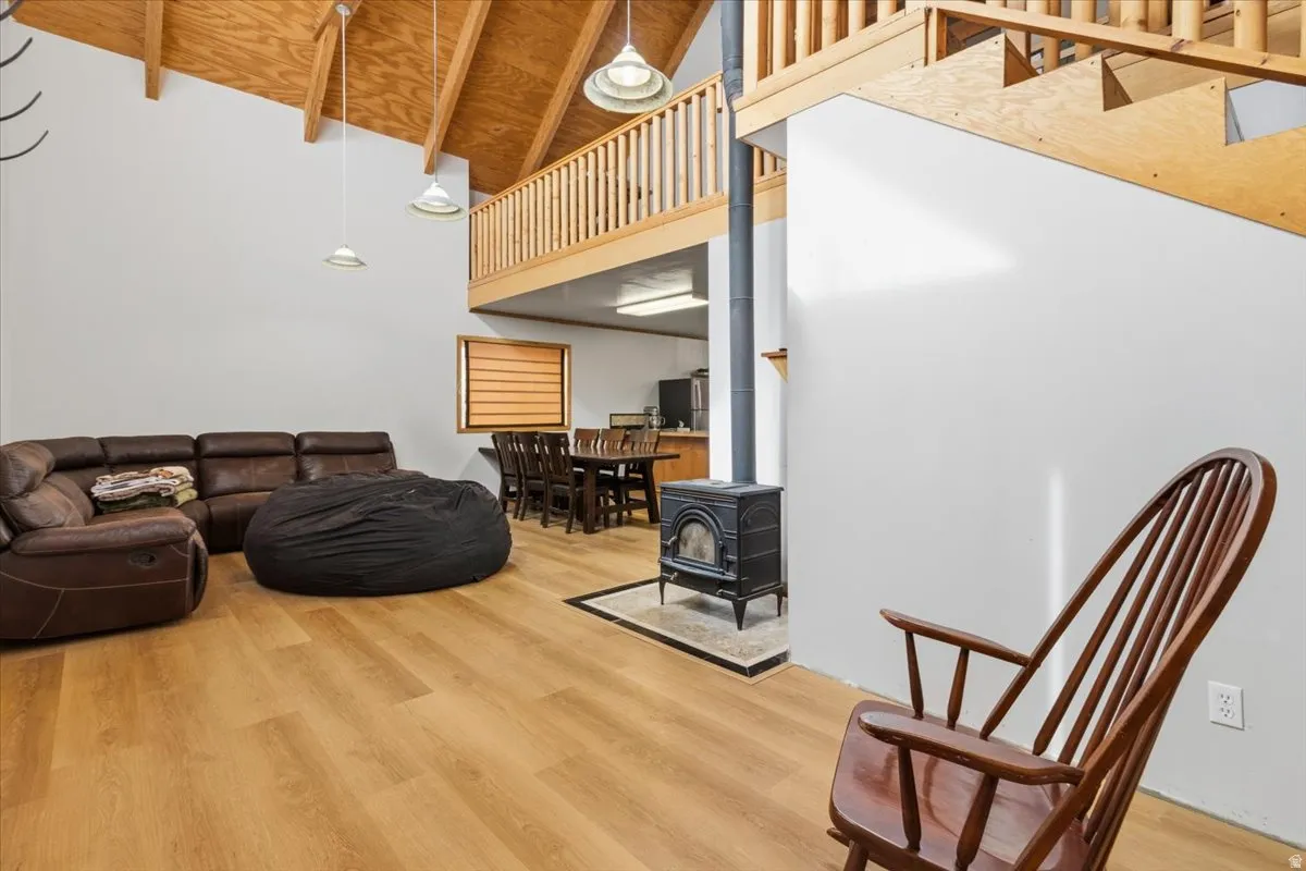 Living area with light wood-style floors, a wood stove, and a high wooden beamed ceiling