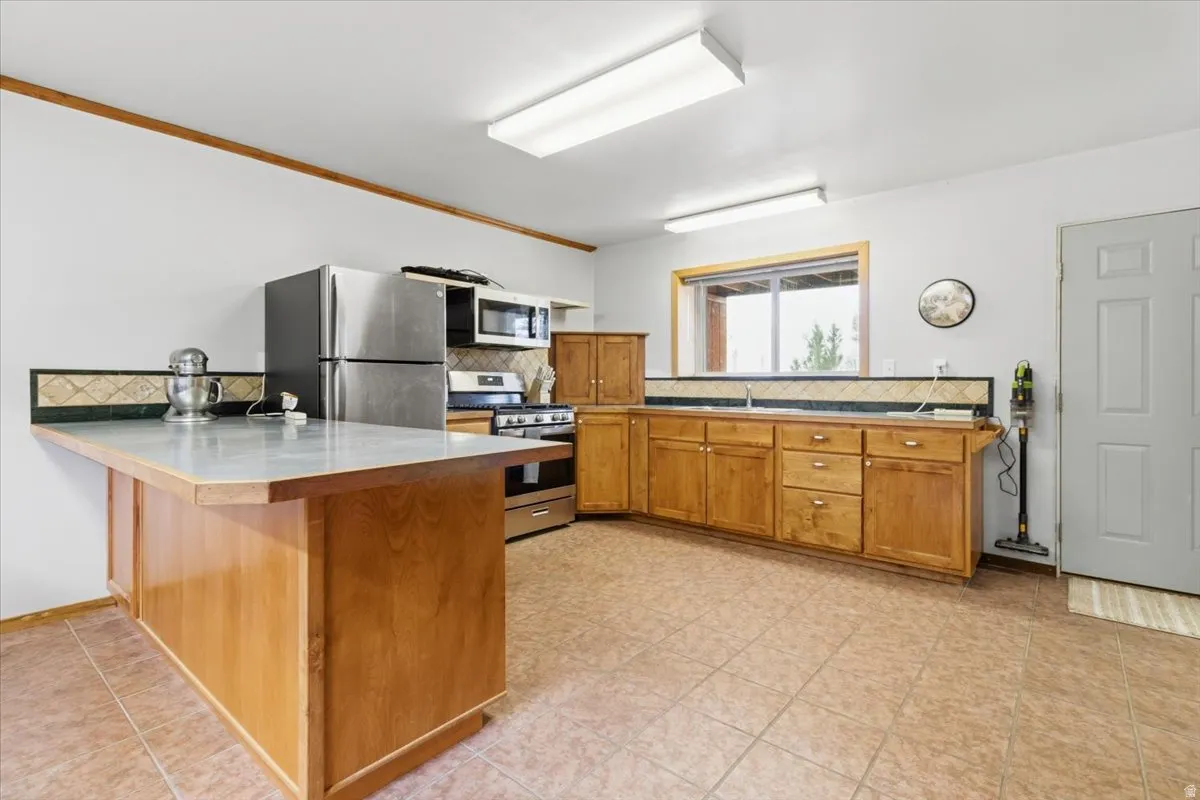 Kitchen featuring a peninsula, decorative backsplash, wood finish cabinetry, stainless steel appliances, and a breakfast bar