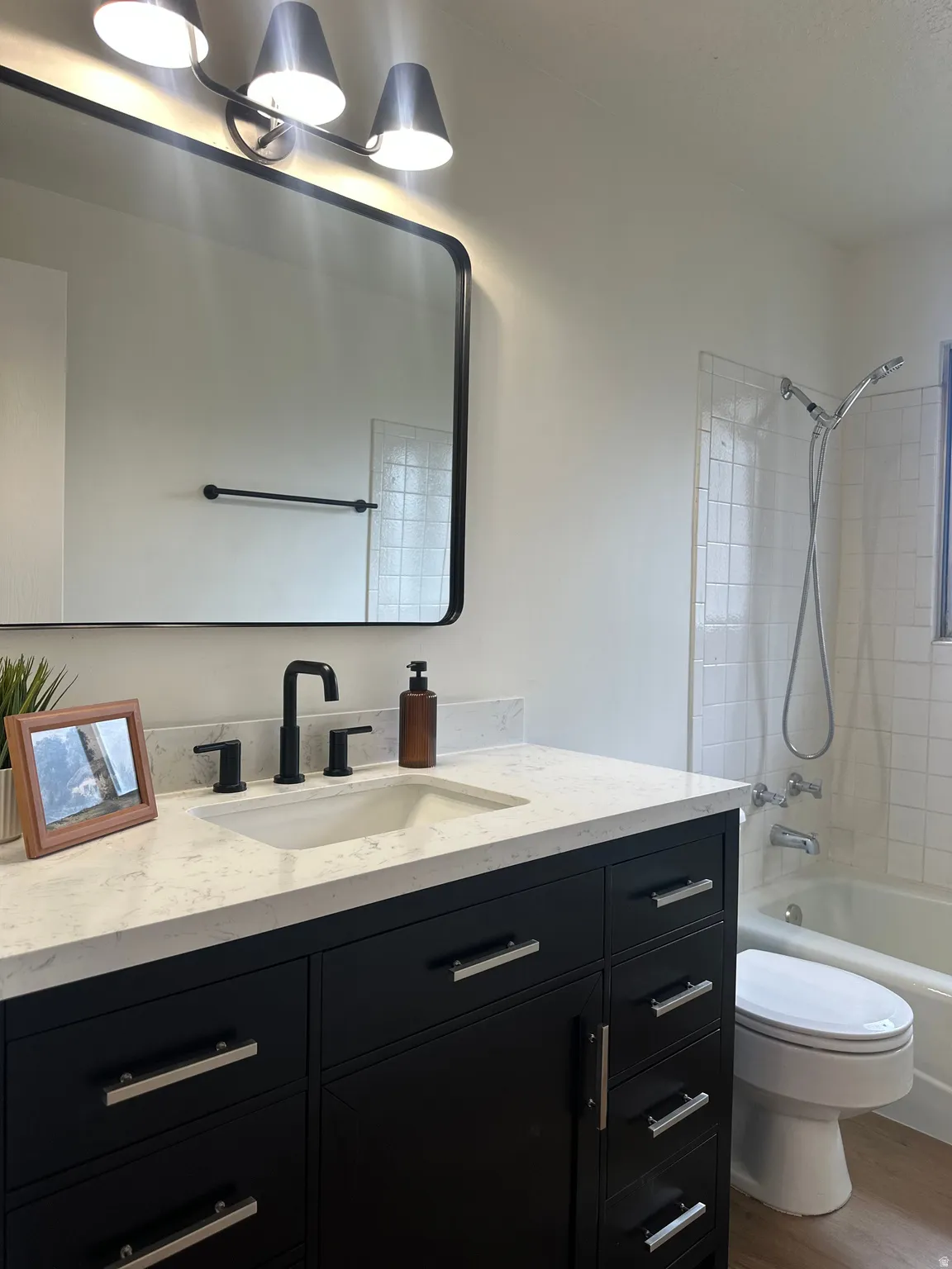 Bathroom featuring a black vanity with silver hardware, an integrated sink, a dark-framed mirror, and a three-light vanity fixture