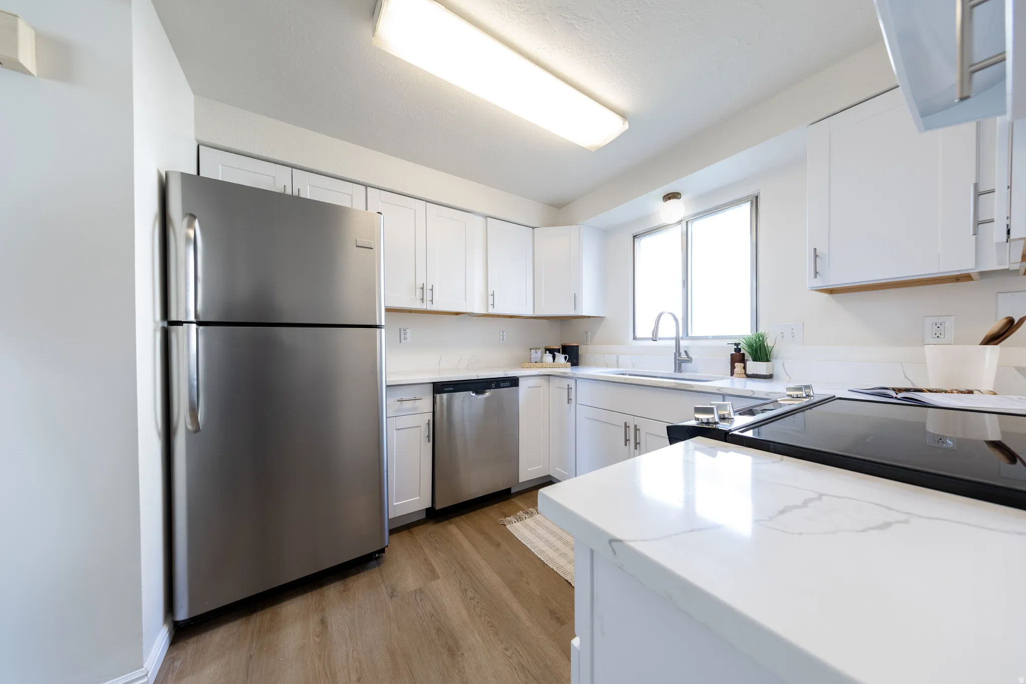 Kitchen featuring stainless steel appliances, light wood-type flooring, white cabinets, and light stone countertops