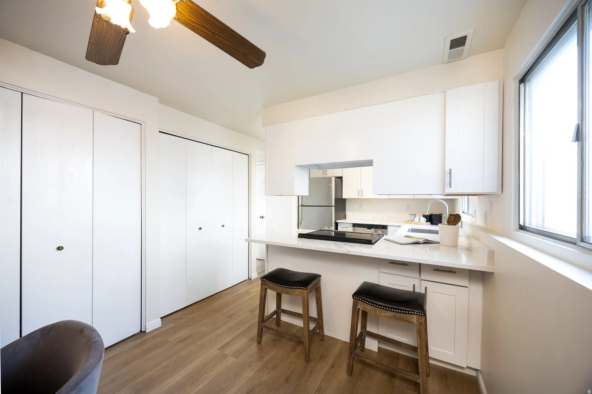 Kitchen with a peninsula, white cabinets, freestanding refrigerator, a kitchen bar, and ceiling fan