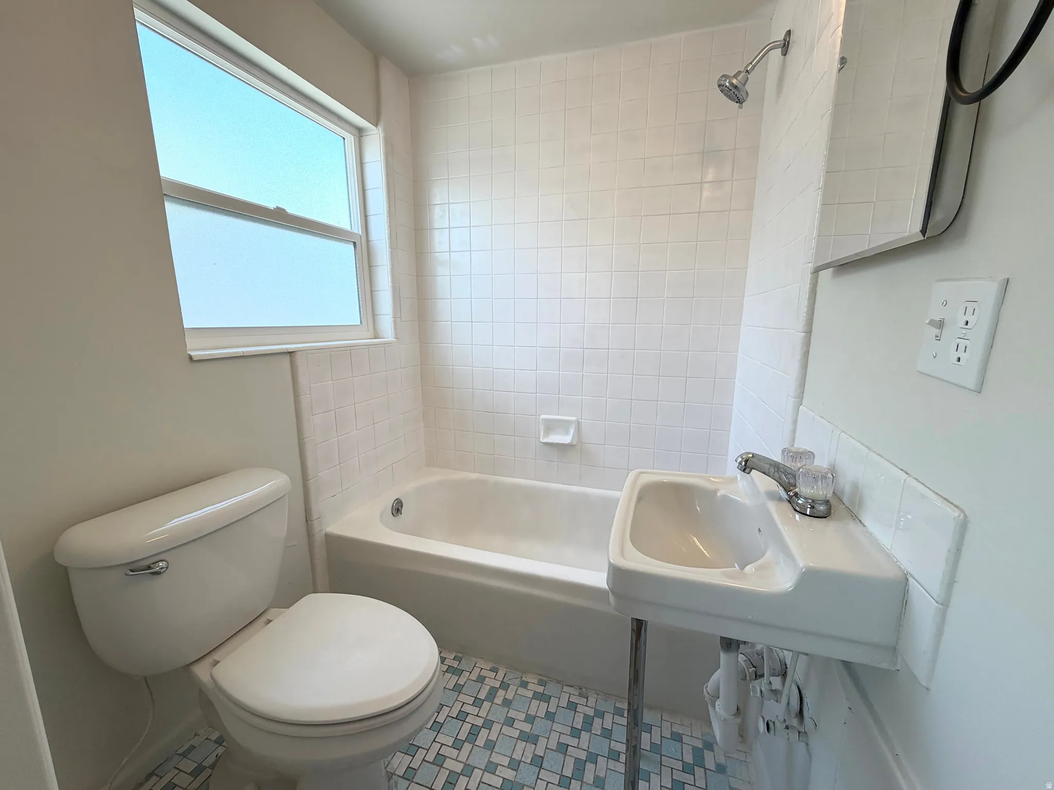 Bathroom featuring a white toilet, white bathtub, white tile shower surround, pedestal sink, and a window