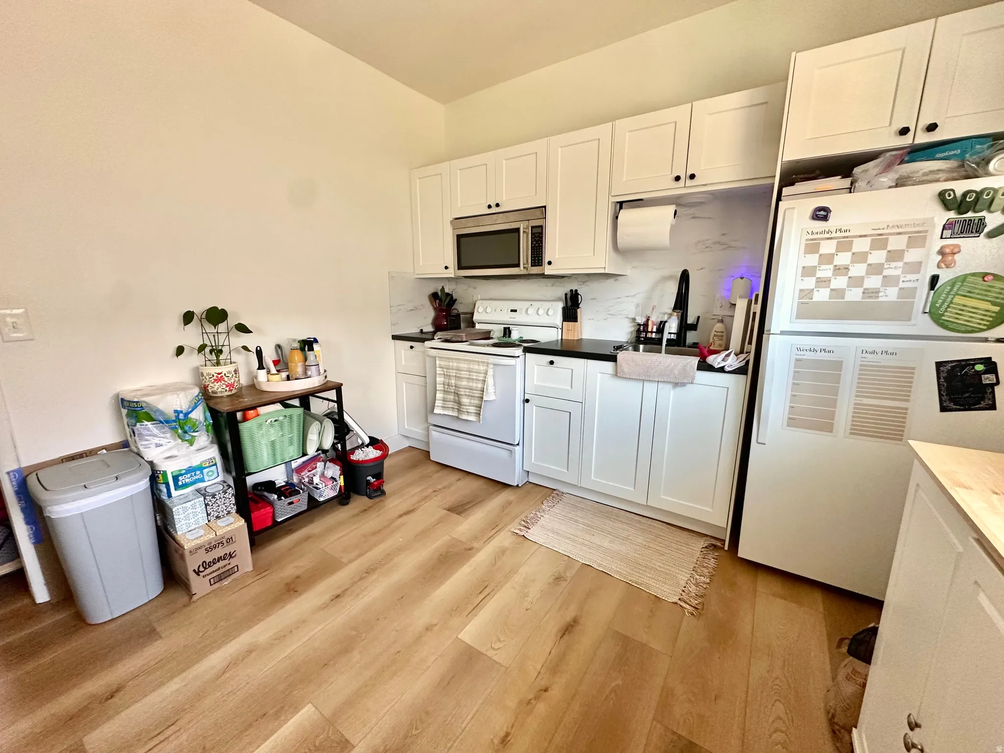 Kitchen featuring white appliances, tasteful backsplash, white cabinets, and light wood finished floors